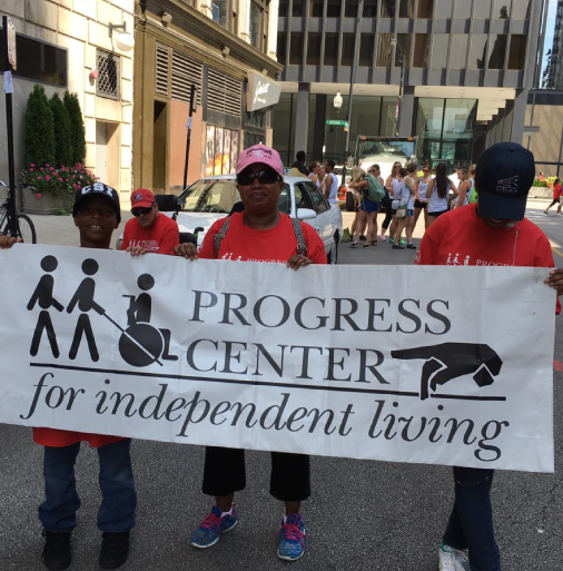 Three Progress Center supporters holding the Progress Center Banner at the Disability Pride Parade