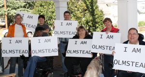 Image of group of people, all holding signs that read "I am Olmstead." 
