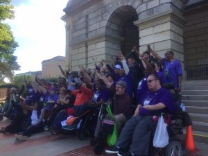 image of group of people standing and in chairs on steps of capitol in Springfield with fists raised