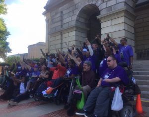 image of group of people standing and in chairs on steps of capitol in Springfield with fists raised