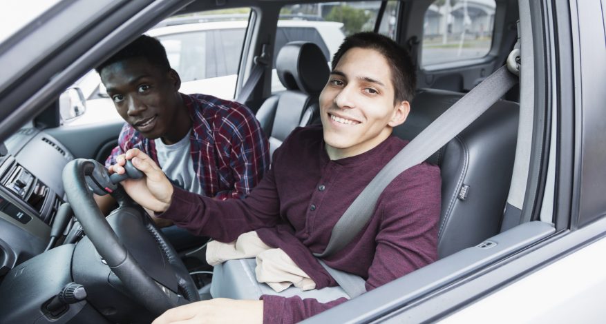 Two friends smiling together in a parking lot. The young man driving is an amputee.