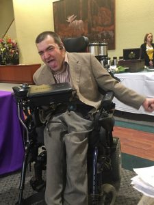 image of caucassion male wearing grey slacks and a tan sport coat, sitting in a power wheelchair