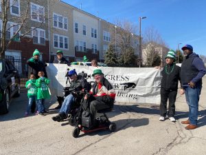 Image from the 2020 Forest Park St. Patrick's Day Parade. Image shows a group of people holding and around a Progress Center banner, lining up for the parade